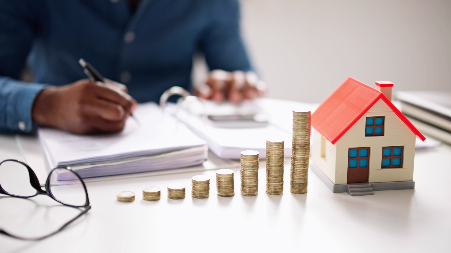 A person sitting at a table with stacks of coins and a model house